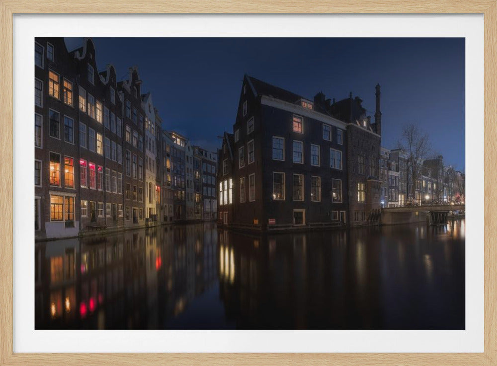 A framed photograph capturing a serene night view of an Amsterdam canal. Traditional Dutch houses with lit windows line the calm water, casting warm reflections under a deep blue twilight sky. Wall Art