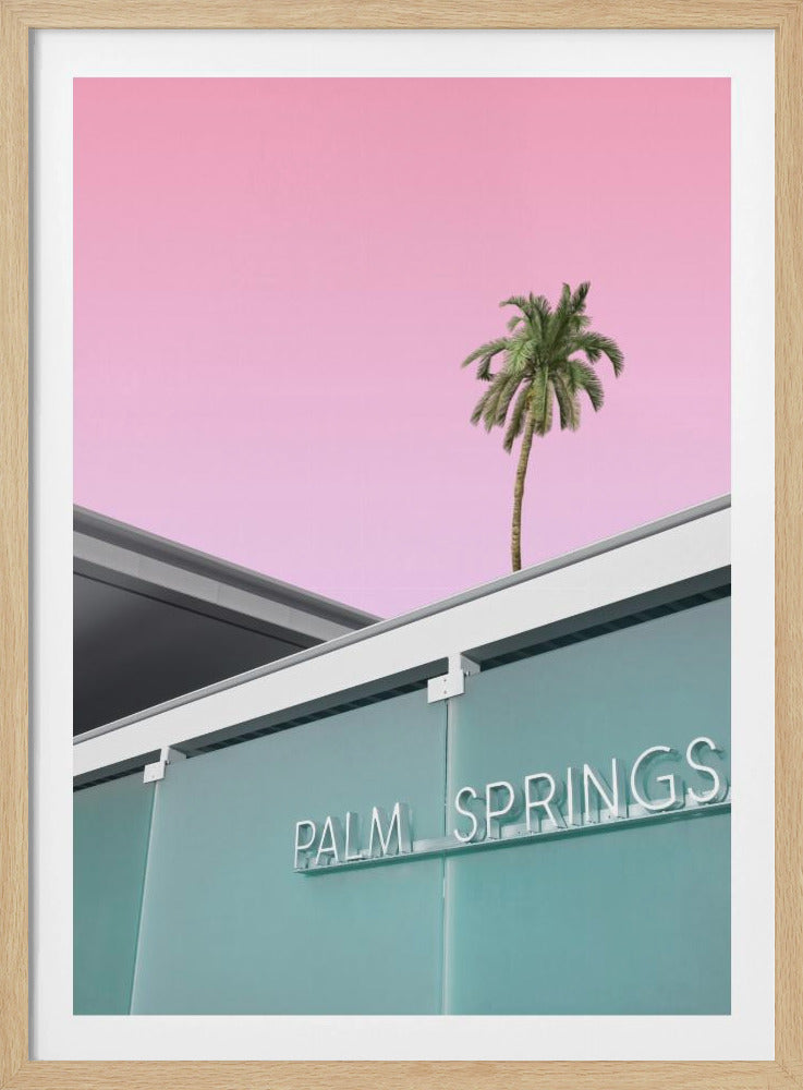 A low-angle shot of a modern building with a frosted teal glass facade and a white neon sign that reads 'PALM SPRINGS'. Above the building, a single tall palm tree stands against a solid, vibrant pink sky, creating a minimalist and stylized composition. Decor