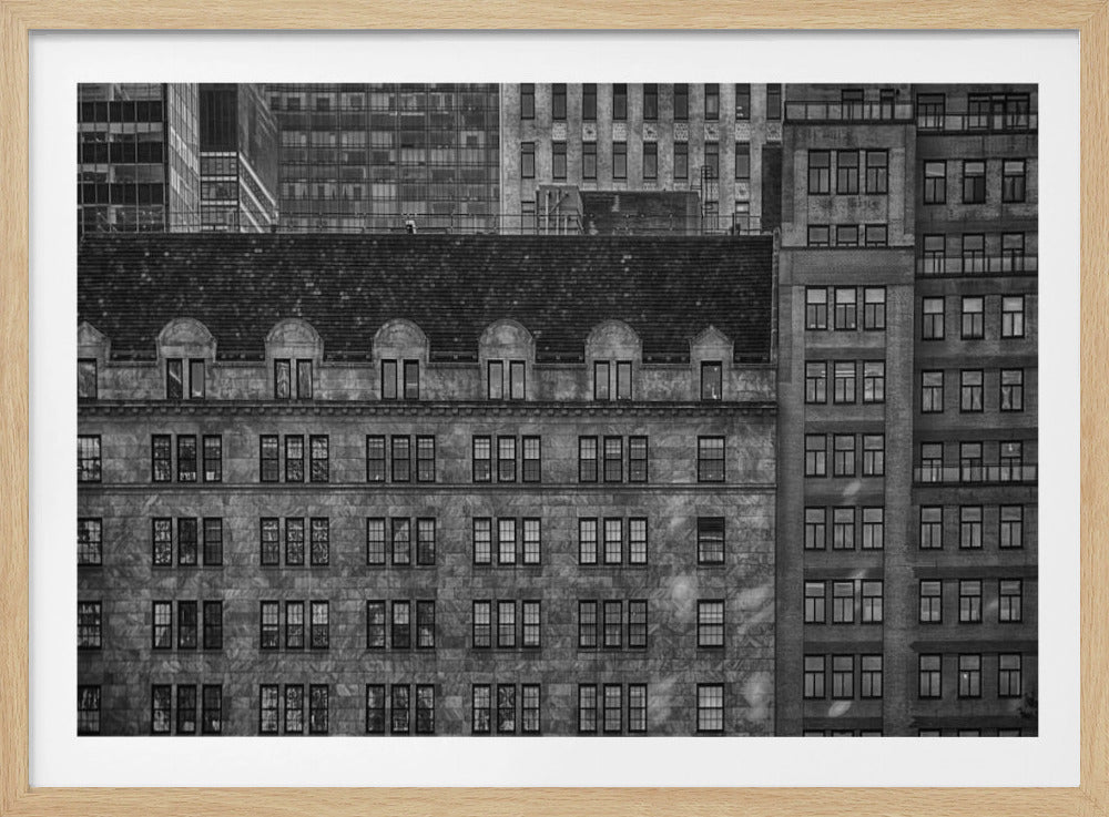 A dense, black and white photograph of various city buildings packed closely together. The image highlights the contrasting architectural styles, from an older stone building with a dark roof in the foreground to taller brick and modern glass buildings in the background, creating a geometric pattern of windows and textures. Decor