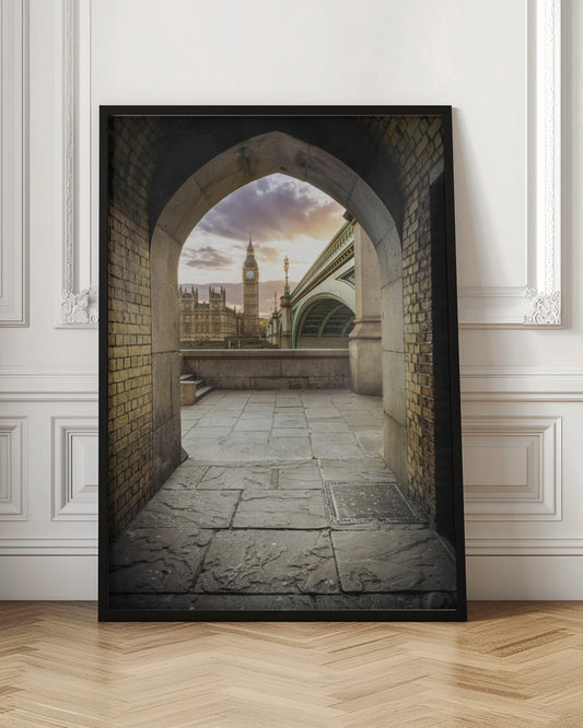A scenic view of London's Big Ben clock tower and the Houses of Parliament as seen through a weathered stone archway. The foreground features a stone-paved walkway, and the background shows the iconic landmarks against a cloudy sunset sky with hues of purple and orange. Poster