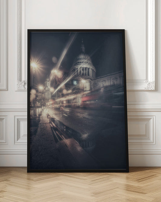 A dynamic long-exposure photograph of a wet London street at night, with the iconic dome of St. Paul's Cathedral illuminated in the background. Streaks of light from passing traffic, including a red bus, blur across the scene, while the glistening pavement reflects the cathedral and bright streetlights. Decor
