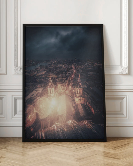 A dramatic, high-angle nighttime photograph of a sprawling city, likely London, viewed from the top of a cathedral. The foreground shows the curved dome, while below, two towers and the long roof of the church are brightly illuminated. The city stretches into the distance with countless golden lights under a dark, stormy, and cloud-filled sky. Poster