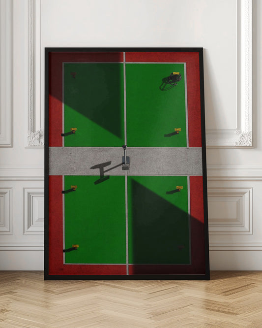 A high-angle, symmetrical photograph of a green and red sports court, viewed from directly above. Strong, sharp shadows cut diagonally across the composition, creating a geometric and abstract pattern of light and dark. A net post in the center casts a T-shaped shadow on the concrete dividing strip. Print