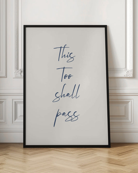 A framed art print featuring the inspirational quote 'This Too shall pass' in a dark blue, elegant cursive script against a simple cream background. The piece is bordered by a thin black frame. Poster