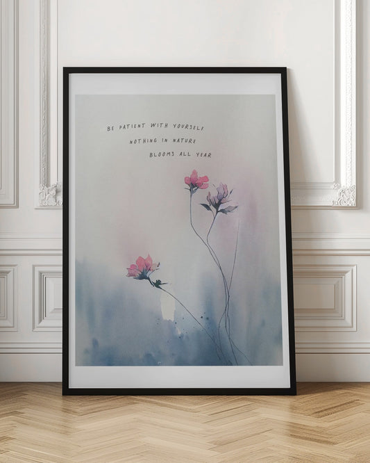 A watercolor painting of delicate pink flowers on thin stems against a soft blue and white background. Above the flowers is the inspirational quote 'Be patient with yourself, nothing in nature blooms all year' in a simple, handwritten font. The artwork is shown in a black frame. Print
