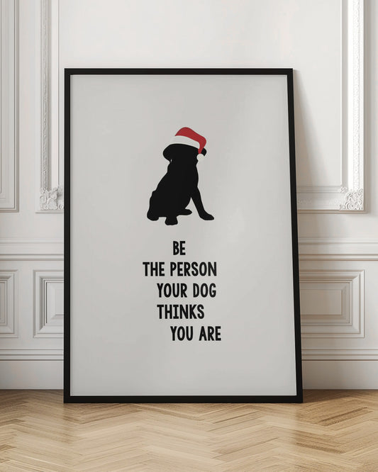 A framed art print featuring a black silhouette of a dog wearing a red Santa hat on an off-white background. Below the dog is the motivational quote, 'BE THE PERSON YOUR DOG THINKS YOU ARE' in black block letters. Decor