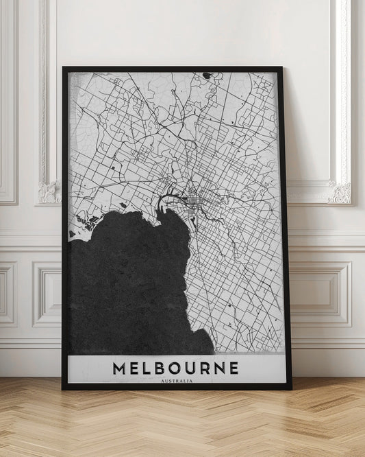 A minimalist black and white map of Melbourne, Australia, presented in a black frame. The city's road network is depicted with fine black lines on a textured white background, while the adjacent bay is shown in solid, textured black. The name 'MELBOURNE' is written in a bold, black font at the bottom. Poster
