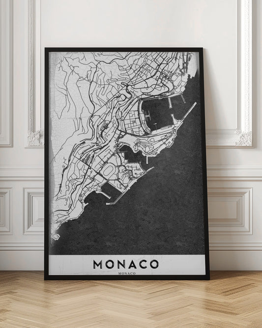 A modern black and white map of Monaco, presented as a framed poster. The map details the city's streets and coastline in black lines on a white background, while the sea is depicted in a solid, textured black. The title 'MONACO' is at the bottom in a bold, white band. Poster