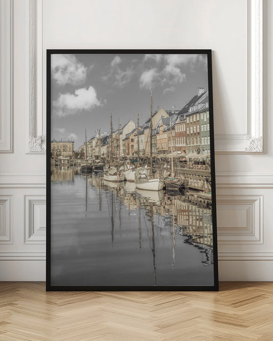 A muted, desaturated photograph of the Nyhavn harbor in Copenhagen. Old-fashioned sailboats are moored along the canal in front of a row of colorful historic buildings. The boats, buildings, and a cloudy sky are perfectly reflected in the calm water. Wall Art