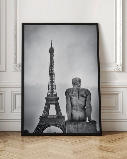 A black and white photograph capturing a contemplative scene in Paris, with the back of a seated, muscular male stone statue in the foreground looking towards the iconic Eiffel Tower which stands tall against a cloudy sky. Print