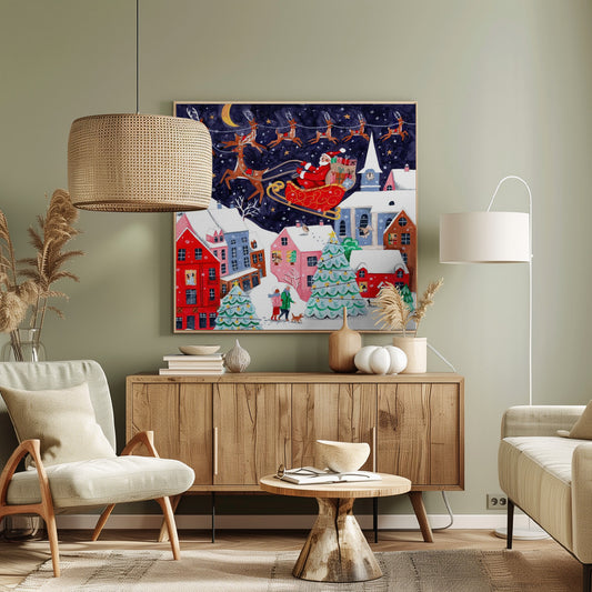 A festive illustration of Santa Claus flying in his sleigh pulled by reindeer over a snowy European-style village at night. The sky is a deep starry blue with a crescent moon, and the houses below are painted in vibrant reds, pinks, and blues, with warm light in the windows. People walk in the snow near decorated Christmas trees. Decor