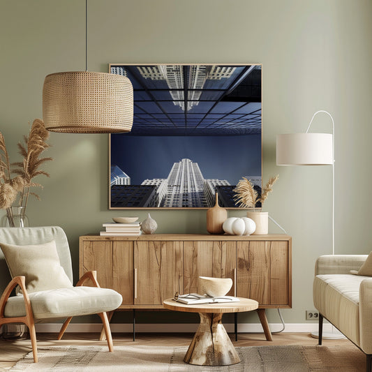 A framed, low-angle photograph capturing a stark white skyscraper against a deep blue sky, with its perfect reflection mirrored in the dark glass facade of an overhanging building, creating a surreal and symmetrical composition. Wall Art