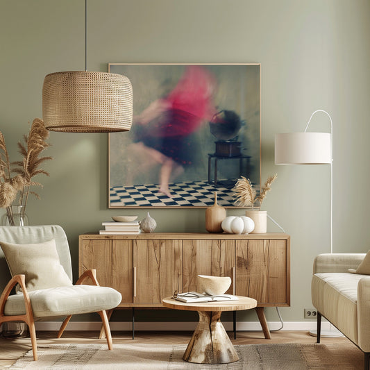 A motion-blurred, artistic photograph in a light wood frame showing a woman dancing barefoot on a black and white checkered floor. She wears a bright red top and a dark skirt, both blurred by her movement. Next to her stands a vintage gramophone on a small table, against a muted, textured wall, creating a dreamy, nostalgic atmosphere. Print