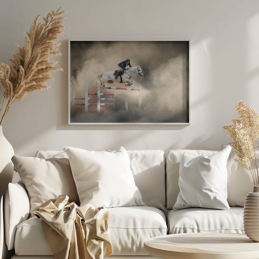 A dramatic action shot of a person in a blue jacket and helmet riding a powerful white horse as it leaps over a red and white striped obstacle, all enveloped in a swirling cloud of brown dust. Print