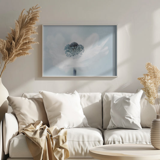 A dreamy, soft-focus macro photograph of a single white anemone flower. The flower has a dark center surrounded by delicate blue-tipped stamens. The background is a soft, pale blue, and the entire image is presented within a silver frame. Wall Art