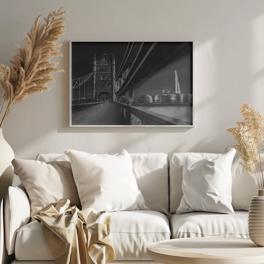 A dramatic, low-angle black and white photograph of London's Tower Bridge at night, taken from the pedestrian walkway. The image showcases the architectural details of the bridge and the illuminated modern city skyline, including The Shard, across the River Thames. Print