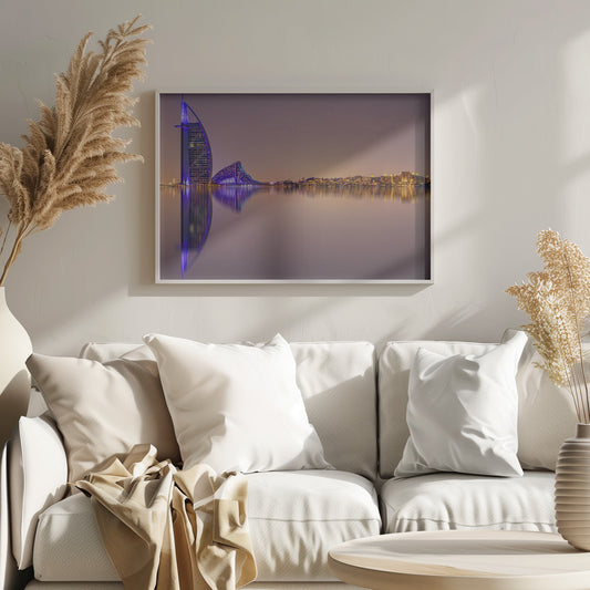 A framed panoramic night photograph of the Dubai skyline featuring the Burj Al Arab hotel lit up in brilliant purple. The city lights and architecture are perfectly reflected in the calm water in the foreground, all under a hazy, dusky sky. Poster