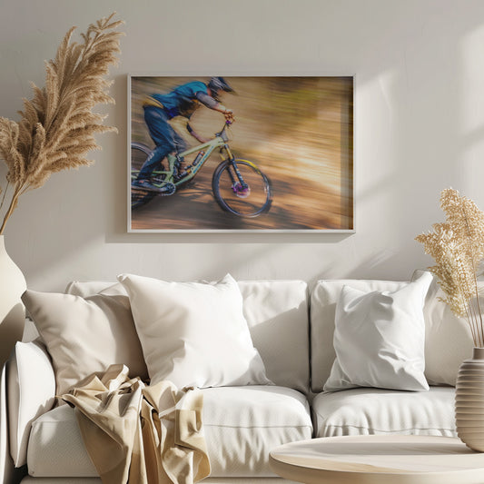 An action shot of a mountain biker in full gear speeding down a dirt trail, captured with a motion blur effect that streaks the brown and green background, conveying a sense of intense speed. Poster