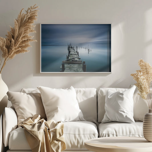 A framed, long exposure photograph of a weathered wooden pier extending into calm, misty blue water under a dramatic, cloudy sky. Wall Art