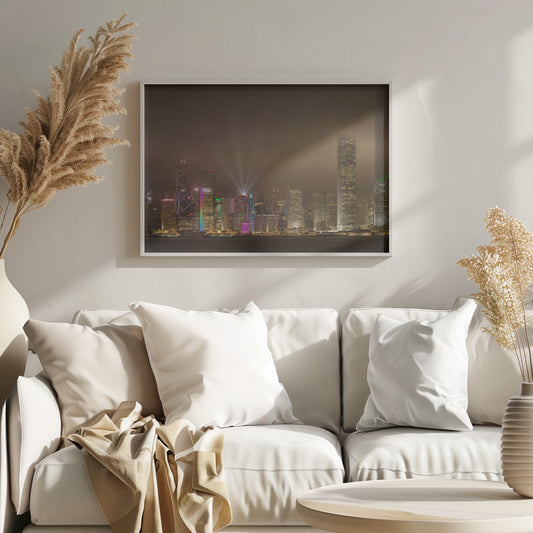 A framed photograph of the Hong Kong skyline at night, viewed from across the water. The skyscrapers are brilliantly lit with yellow, white, and colorful lights, and beams of light shoot up into the foggy, glowing sky. Decor