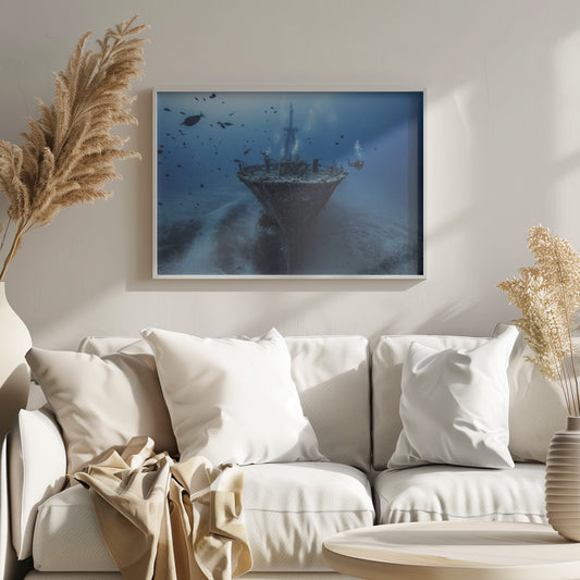 An underwater photograph of a large, sunken shipwreck resting on the sandy ocean floor. Two scuba divers are exploring the wreck, surrounded by schools of small fish in the deep blue water, with light filtering down from the surface. Print