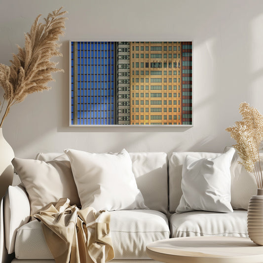 An abstract architectural photograph showing the colorful gridded facades of three adjacent skyscrapers, featuring a blue-windowed building, a white building, and a yellow building, all contained within a silver frame. Wall Art
