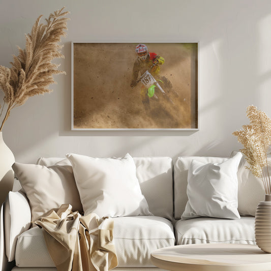 An action shot of a motocross rider in full red and yellow gear, speeding through a dirt track and kicking up a large cloud of brown dust and debris. Print
