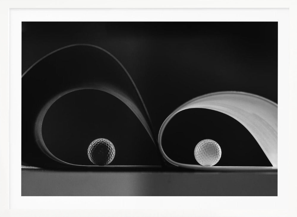 A framed, black and white abstract photograph featuring two golf balls nestled within the graceful curves of a single sheet of paper, creating a striking interplay of light, shadow, and form against a dark background. Decor