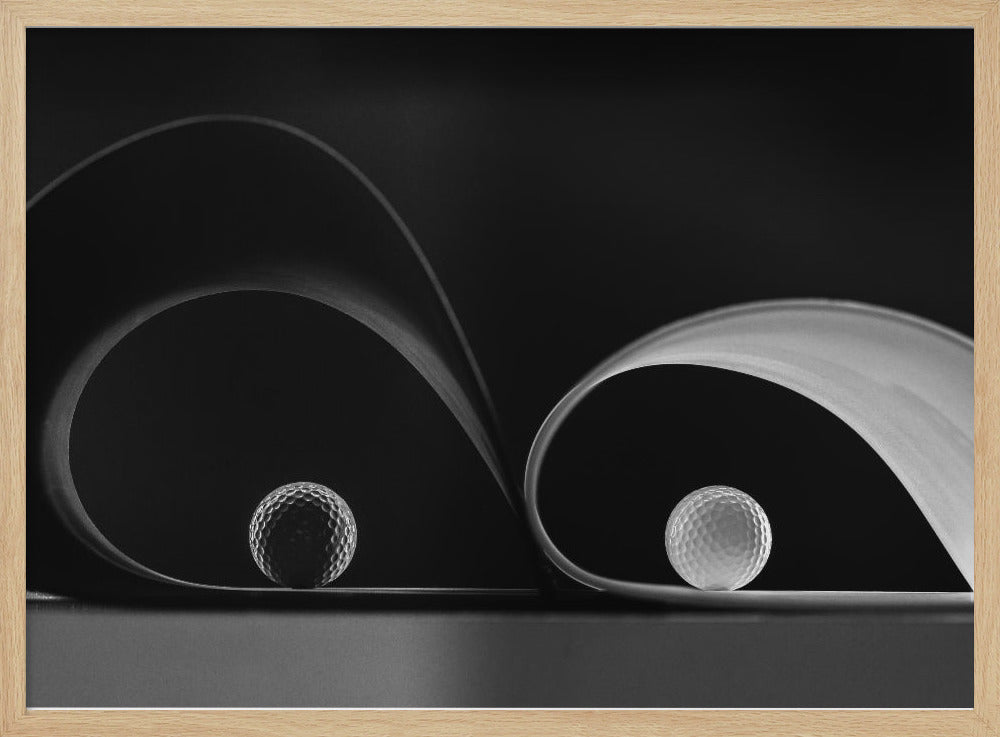 A framed, black and white abstract photograph featuring two golf balls nestled within the graceful curves of a single sheet of paper, creating a striking interplay of light, shadow, and form against a dark background. Decor