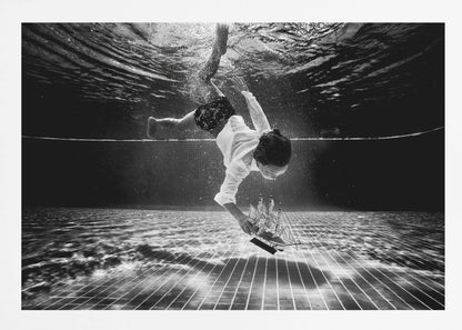 A surreal black and white underwater photograph of a child in a white shirt and shorts diving towards the bottom of a tiled pool to retrieve a miniature model of a sailing ship. Artwork