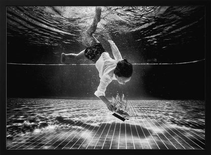 A surreal black and white underwater photograph of a child in a white shirt and shorts diving towards the bottom of a tiled pool to retrieve a miniature model of a sailing ship. Artwork