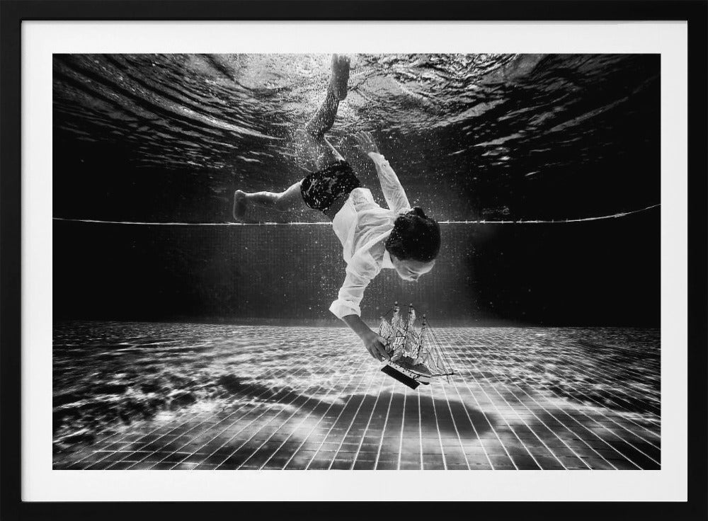 A surreal black and white underwater photograph of a child in a white shirt and shorts diving towards the bottom of a tiled pool to retrieve a miniature model of a sailing ship. Artwork
