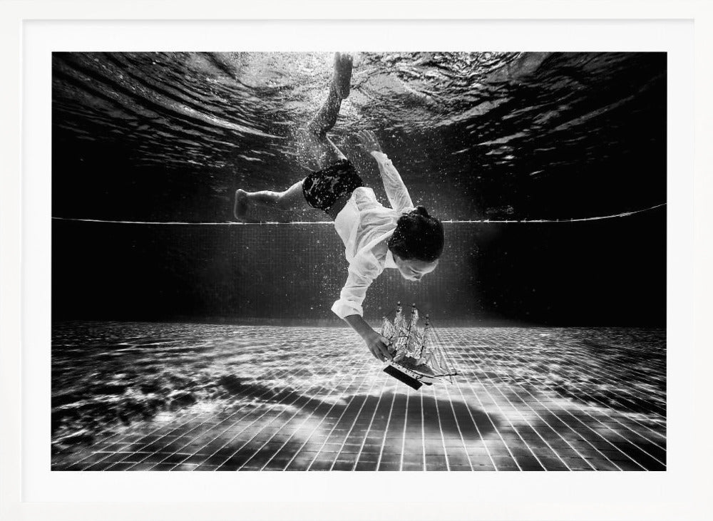 A surreal black and white underwater photograph of a child in a white shirt and shorts diving towards the bottom of a tiled pool to retrieve a miniature model of a sailing ship. Artwork