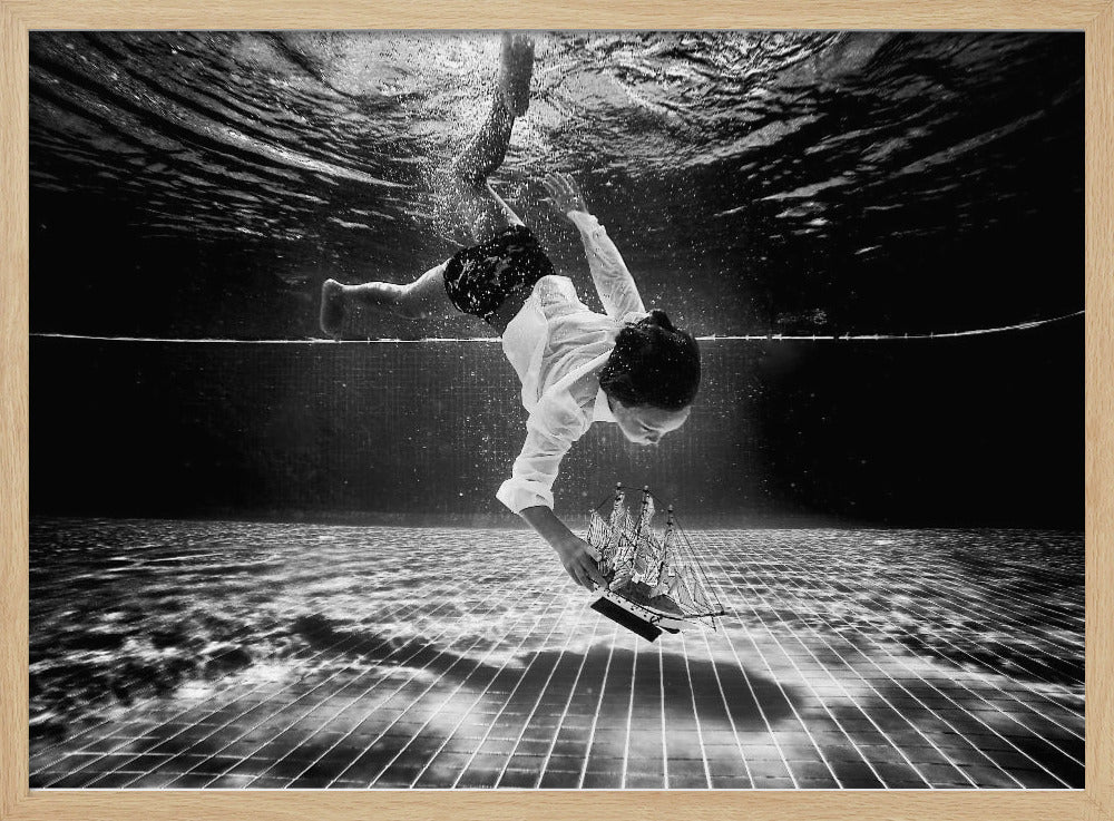 A surreal black and white underwater photograph of a child in a white shirt and shorts diving towards the bottom of a tiled pool to retrieve a miniature model of a sailing ship. Artwork