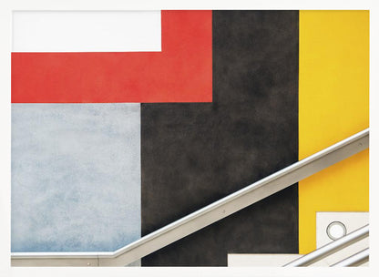 A framed abstract art piece featuring a composition of large, solid-colored geometric shapes in red, yellow, black, white, and light gray. A silver handrail cuts diagonally across the lower portion of the image, adding a sharp line and a sense of architectural space. Artwork