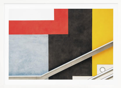 A framed abstract art piece featuring a composition of large, solid-colored geometric shapes in red, yellow, black, white, and light gray. A silver handrail cuts diagonally across the lower portion of the image, adding a sharp line and a sense of architectural space. Artwork