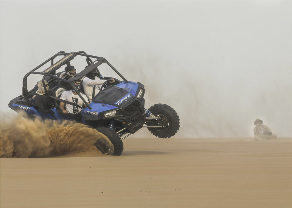 A framed action shot of a blue dune buggy with several passengers making a sharp turn in the desert, kicking up a large cloud of sand and lifting its front wheel off the ground. Wall Art