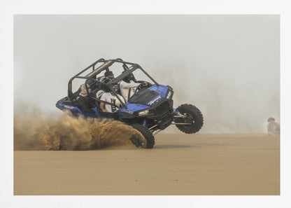 A framed action shot of a blue dune buggy with several passengers making a sharp turn in the desert, kicking up a large cloud of sand and lifting its front wheel off the ground. Wall Art