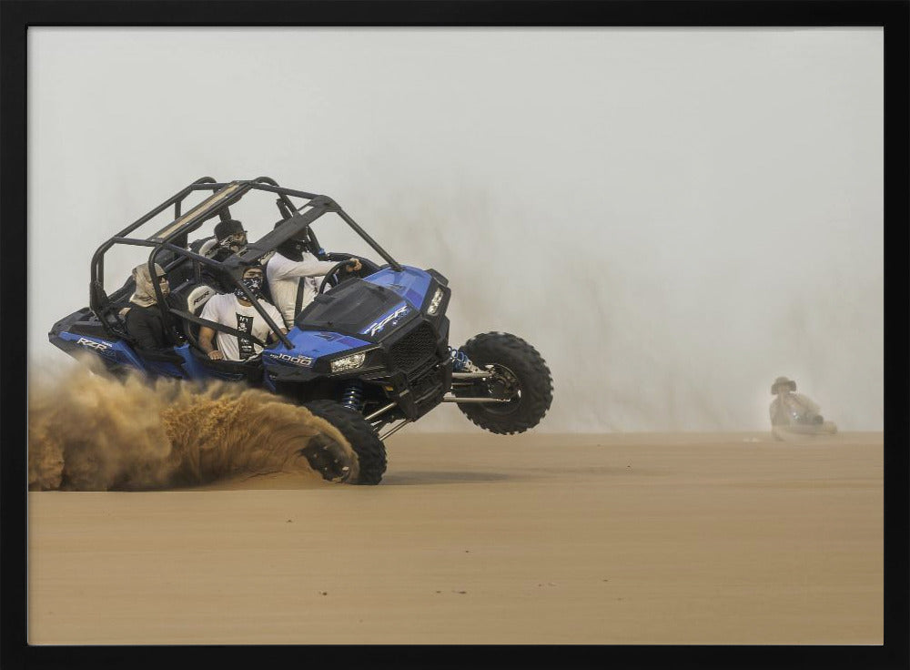 A framed action shot of a blue dune buggy with several passengers making a sharp turn in the desert, kicking up a large cloud of sand and lifting its front wheel off the ground. Wall Art