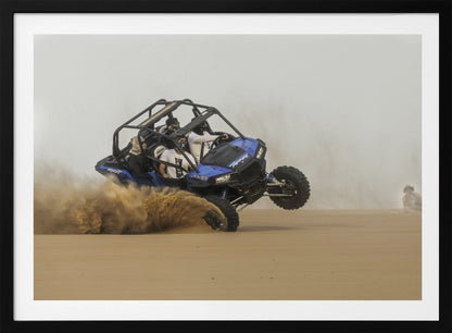A framed action shot of a blue dune buggy with several passengers making a sharp turn in the desert, kicking up a large cloud of sand and lifting its front wheel off the ground. Wall Art