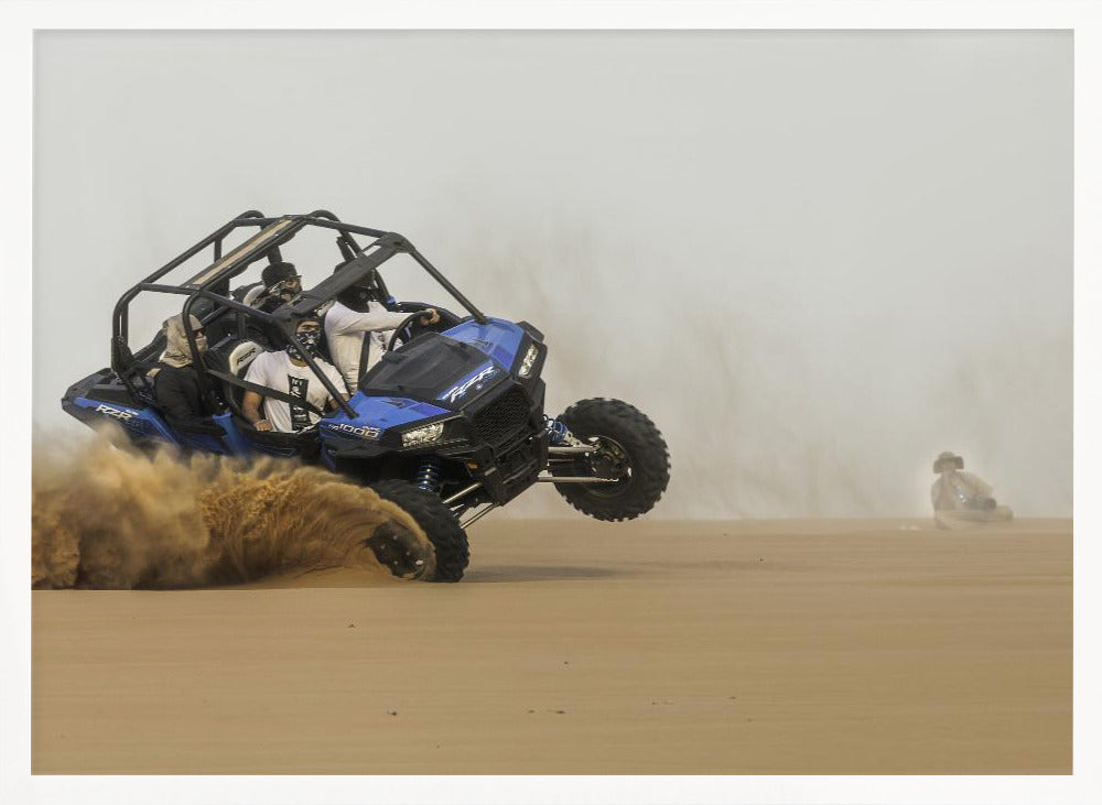 A framed action shot of a blue dune buggy with several passengers making a sharp turn in the desert, kicking up a large cloud of sand and lifting its front wheel off the ground. Wall Art