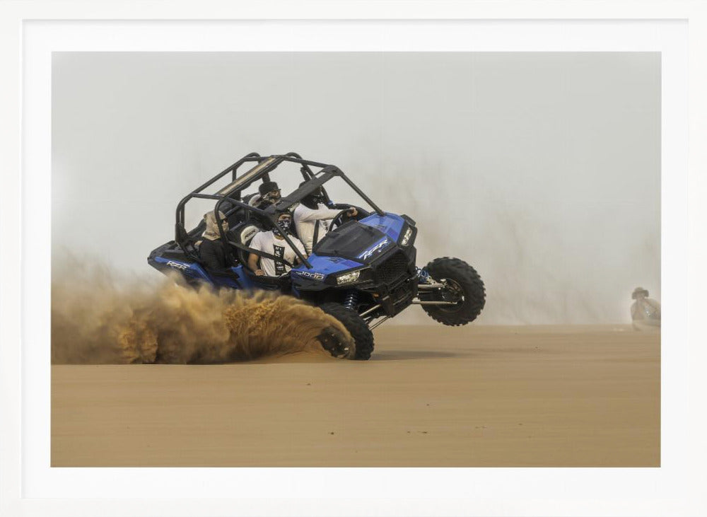 A framed action shot of a blue dune buggy with several passengers making a sharp turn in the desert, kicking up a large cloud of sand and lifting its front wheel off the ground. Wall Art