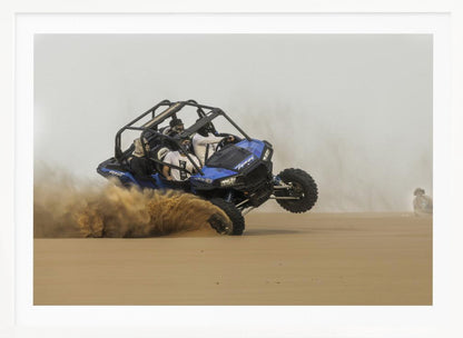 A framed action shot of a blue dune buggy with several passengers making a sharp turn in the desert, kicking up a large cloud of sand and lifting its front wheel off the ground. Wall Art