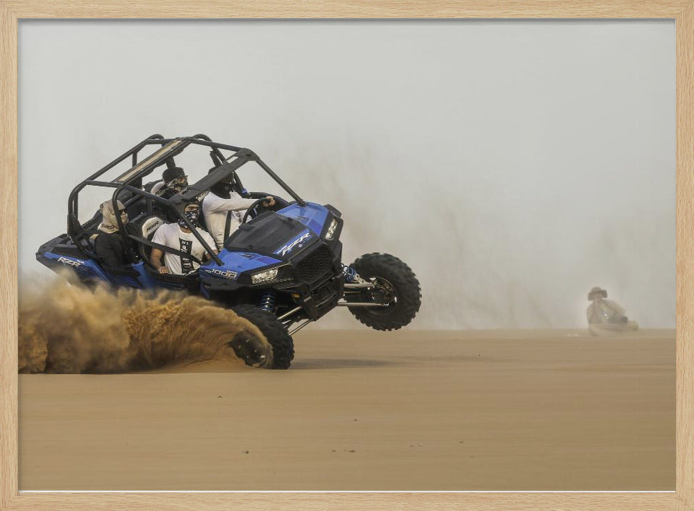 A framed action shot of a blue dune buggy with several passengers making a sharp turn in the desert, kicking up a large cloud of sand and lifting its front wheel off the ground. Wall Art