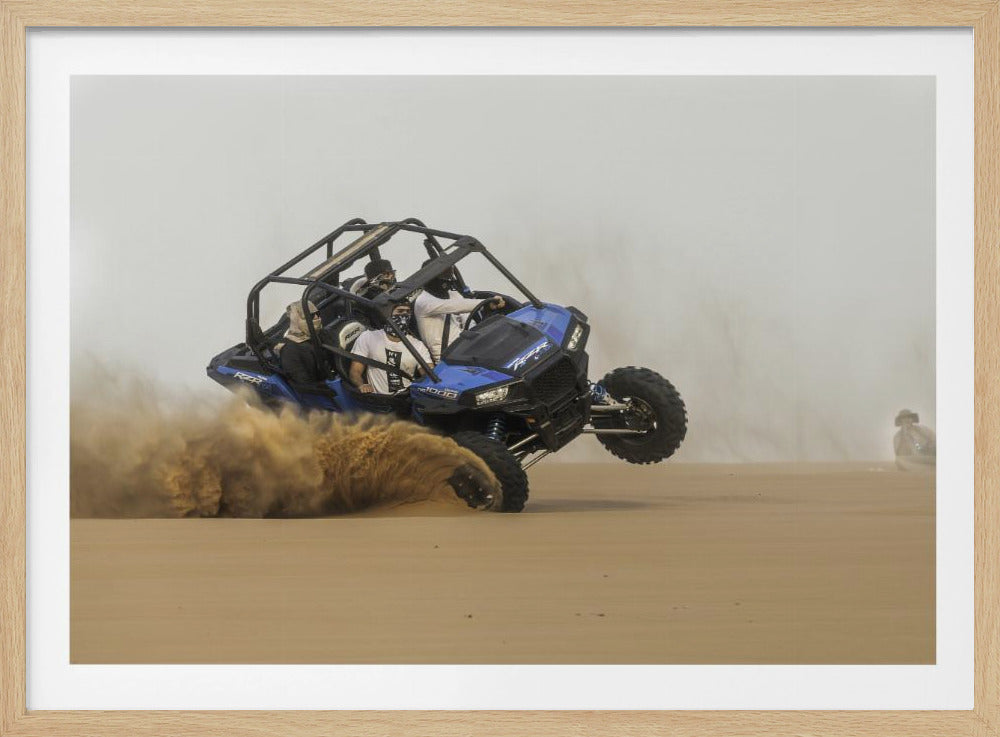 A framed action shot of a blue dune buggy with several passengers making a sharp turn in the desert, kicking up a large cloud of sand and lifting its front wheel off the ground. Wall Art