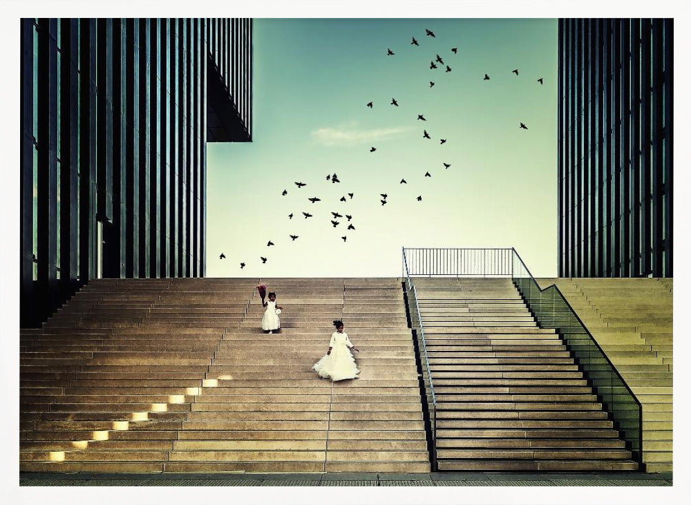 A framed piece of art depicting two young girls in white dresses climbing a vast, modern concrete staircase flanked by two towering, dark buildings. A large flock of birds flies through the teal sky above them, adding a sense of movement to the structured, architectural scene. Poster