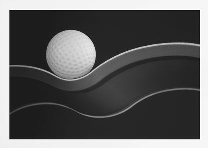 A framed, minimalist black and white photograph of a golf ball resting on a gracefully curving gray surface against a solid black background. Wall Art