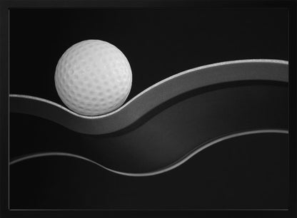 A framed, minimalist black and white photograph of a golf ball resting on a gracefully curving gray surface against a solid black background. Wall Art