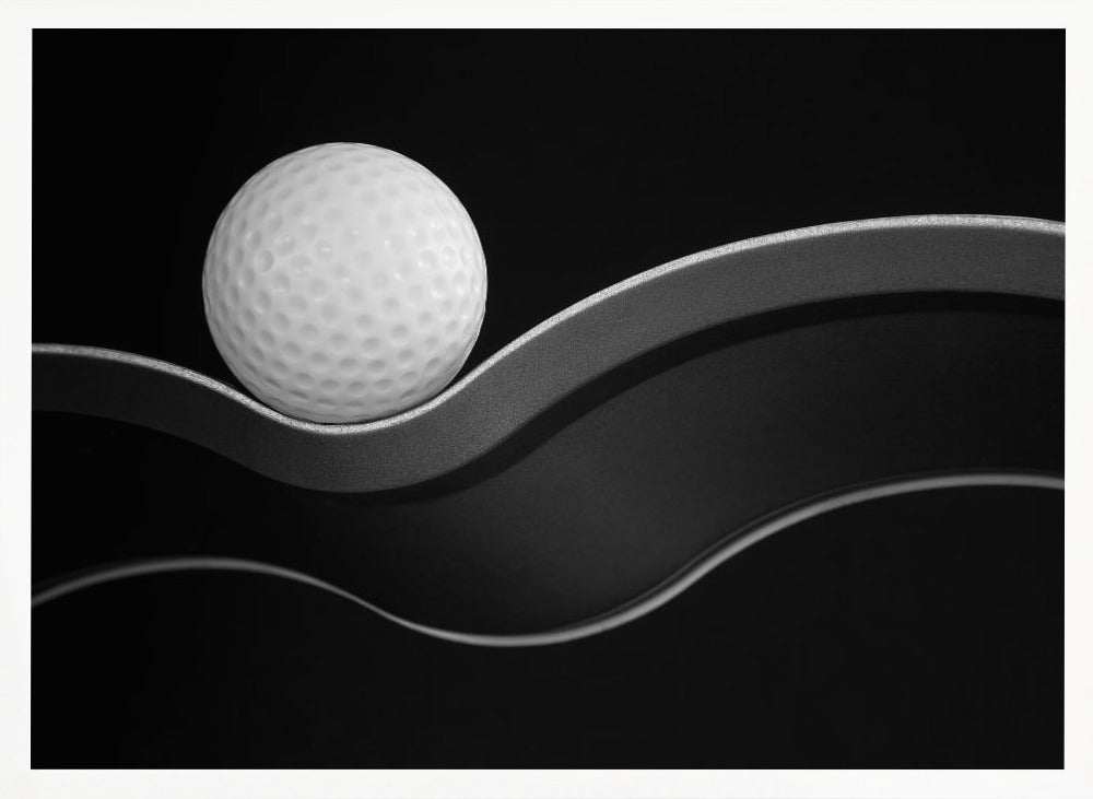 A framed, minimalist black and white photograph of a golf ball resting on a gracefully curving gray surface against a solid black background. Wall Art