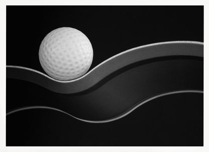 A framed, minimalist black and white photograph of a golf ball resting on a gracefully curving gray surface against a solid black background. Wall Art